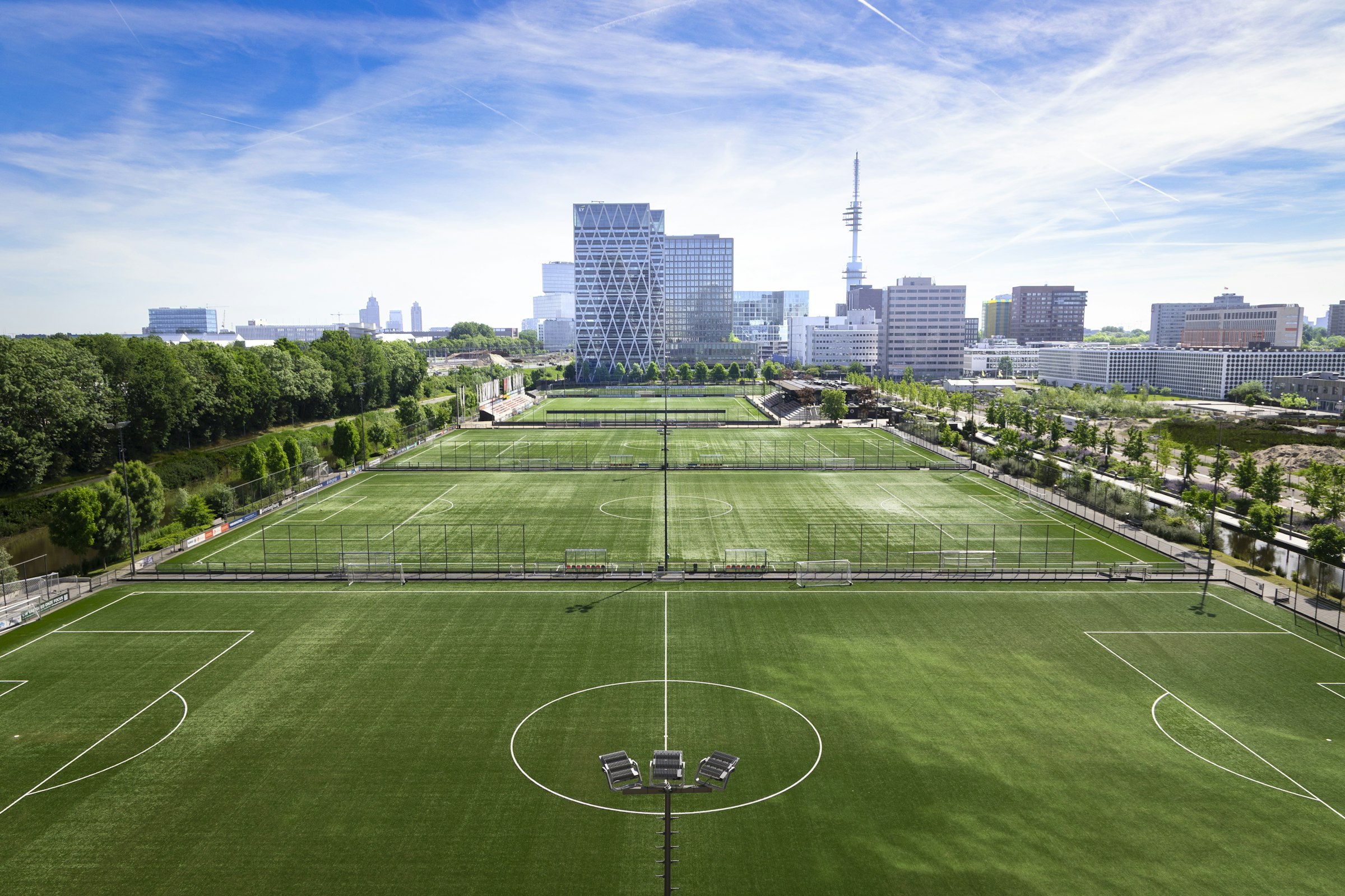 Football pitches in the foreground and the glass towers of Amsterdam's Zuidas business district behind them.