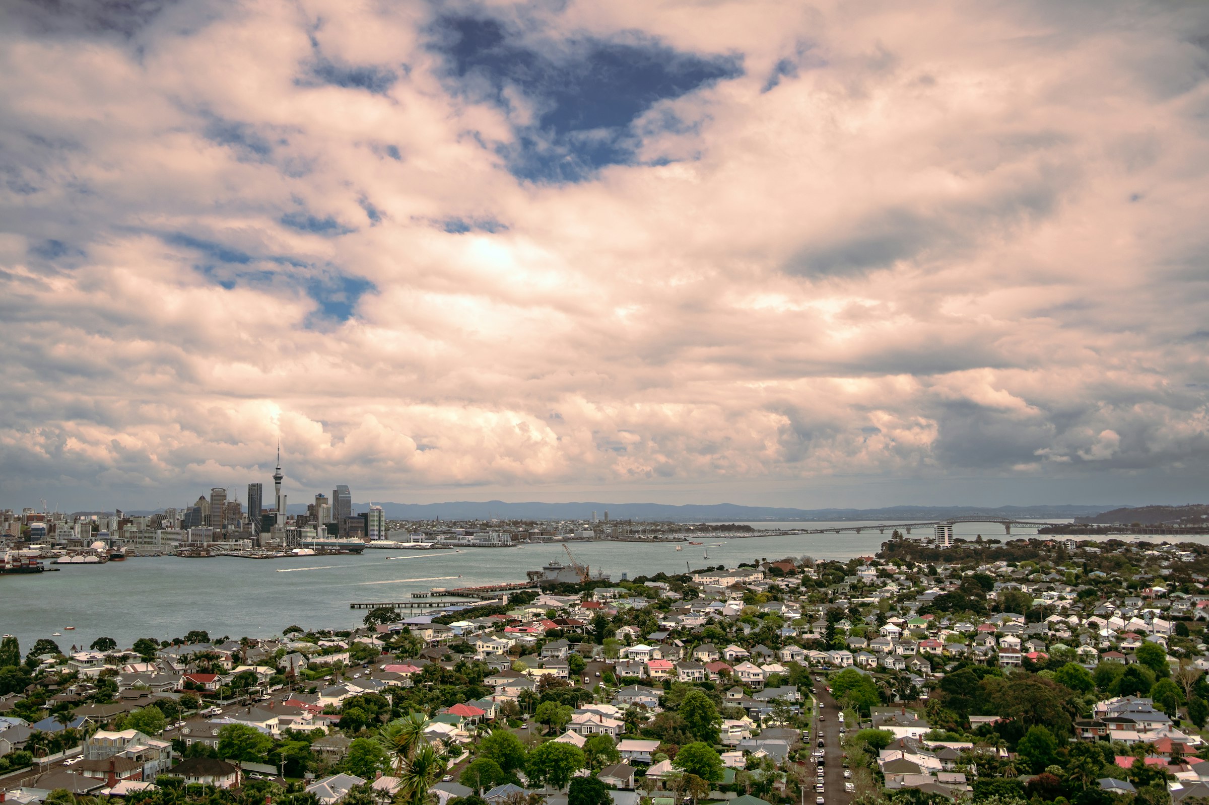 The rooftops of Devonport below a wide sky, the harbour, the city skyline and the Harbour Bridge in the distance.