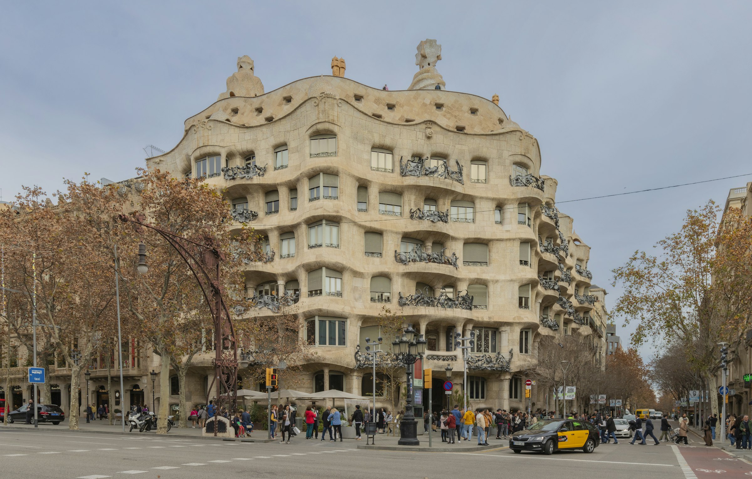 Gaudí's La Pedrera, a wavy stone apartment building on a street corner lined with bare plane trees.