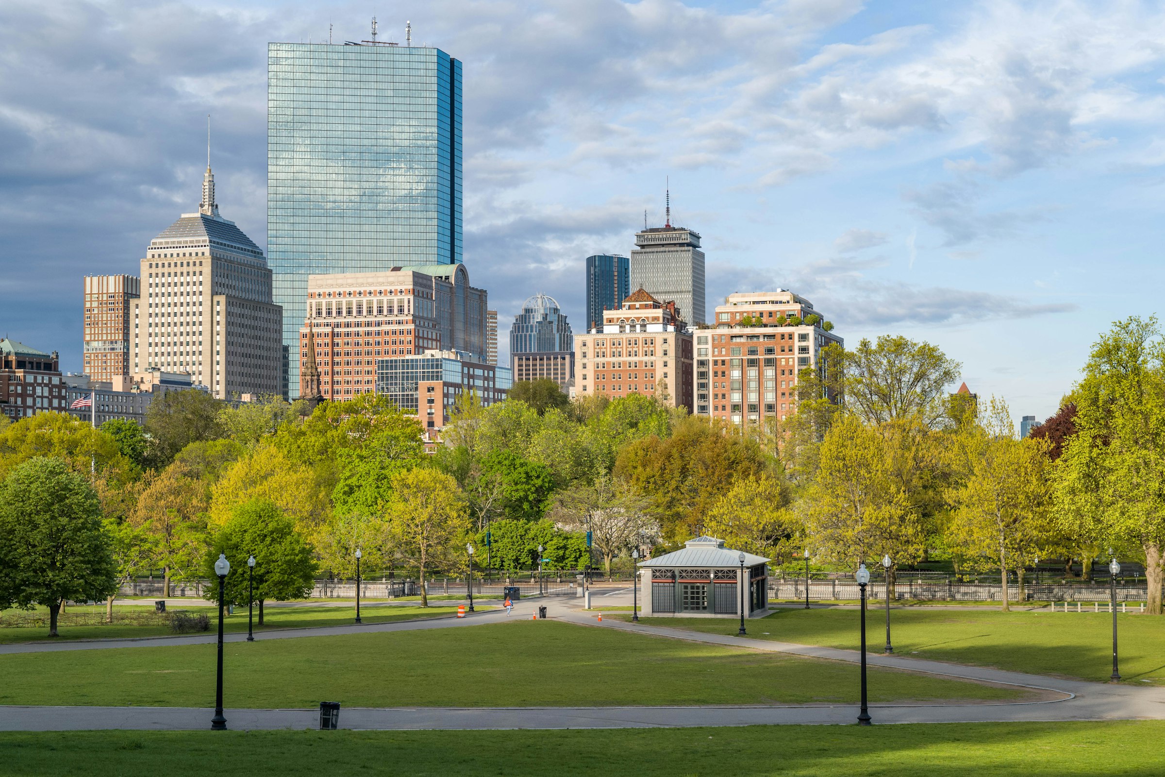 The open grass of Boston Common with the city's buildings beyond it under a blue sky.