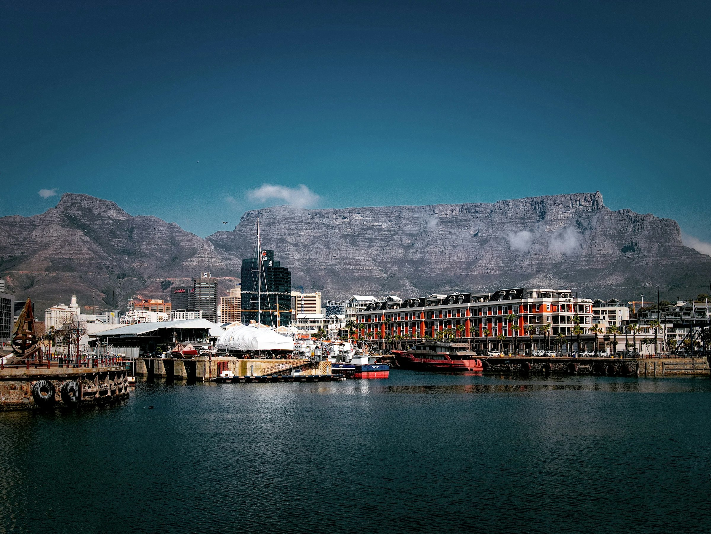 The V&A Waterfront harbour with its red-brick buildings and boats, Table Mountain and Devil's Peak behind under cloud.