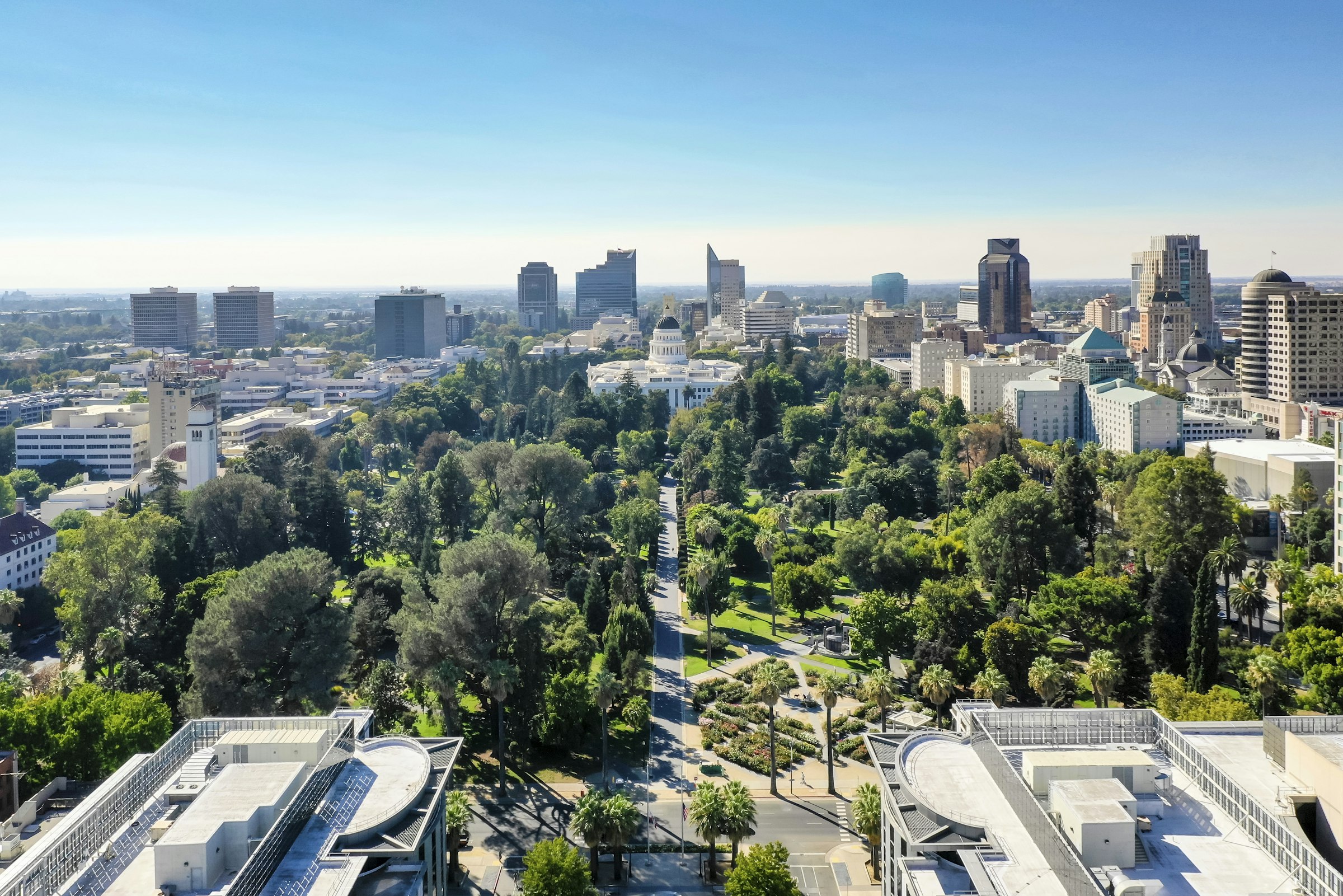 A long tree-filled park leading to the domed State Capitol, with downtown office towers behind it.