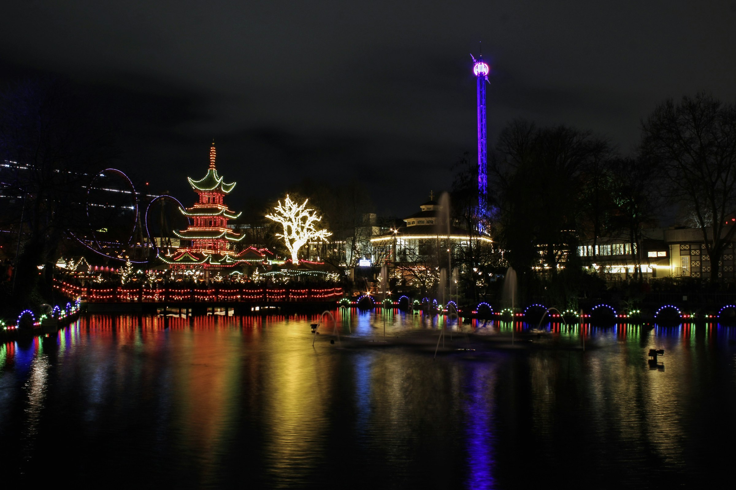 A pagoda and fairground lights reflected in a lake at night in Tivoli Gardens.
