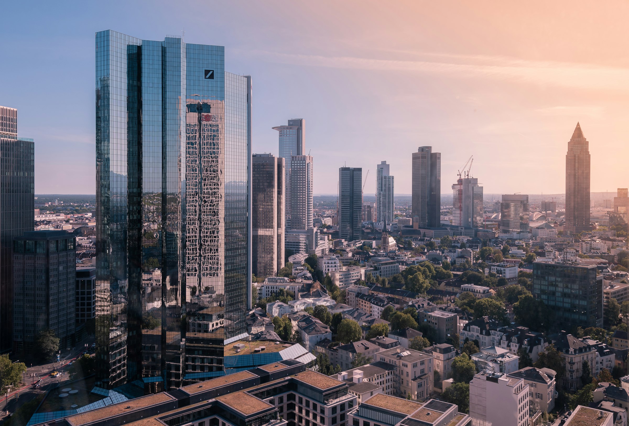 Frankfurt's skyscrapers seen from above in warm evening light, the pointed Messeturm on the right.