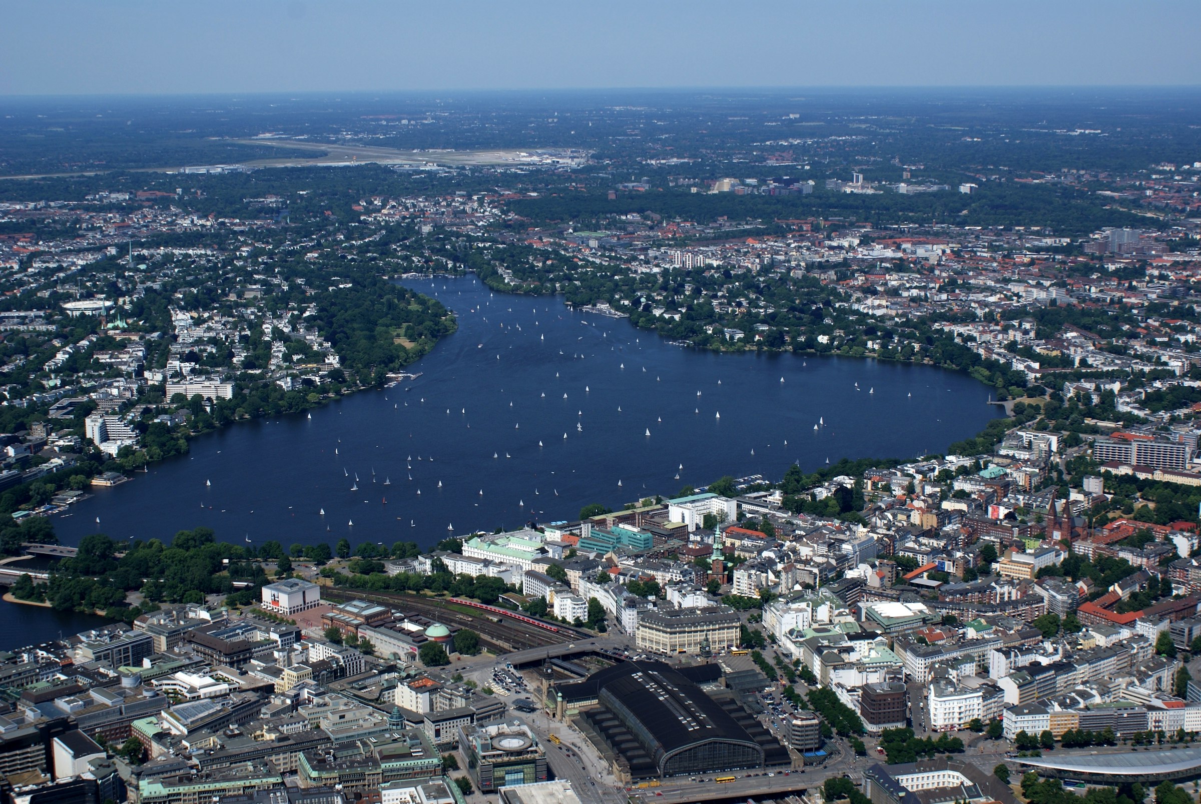 An aerial view of a large lake in the middle of a city, dotted with sailing boats.