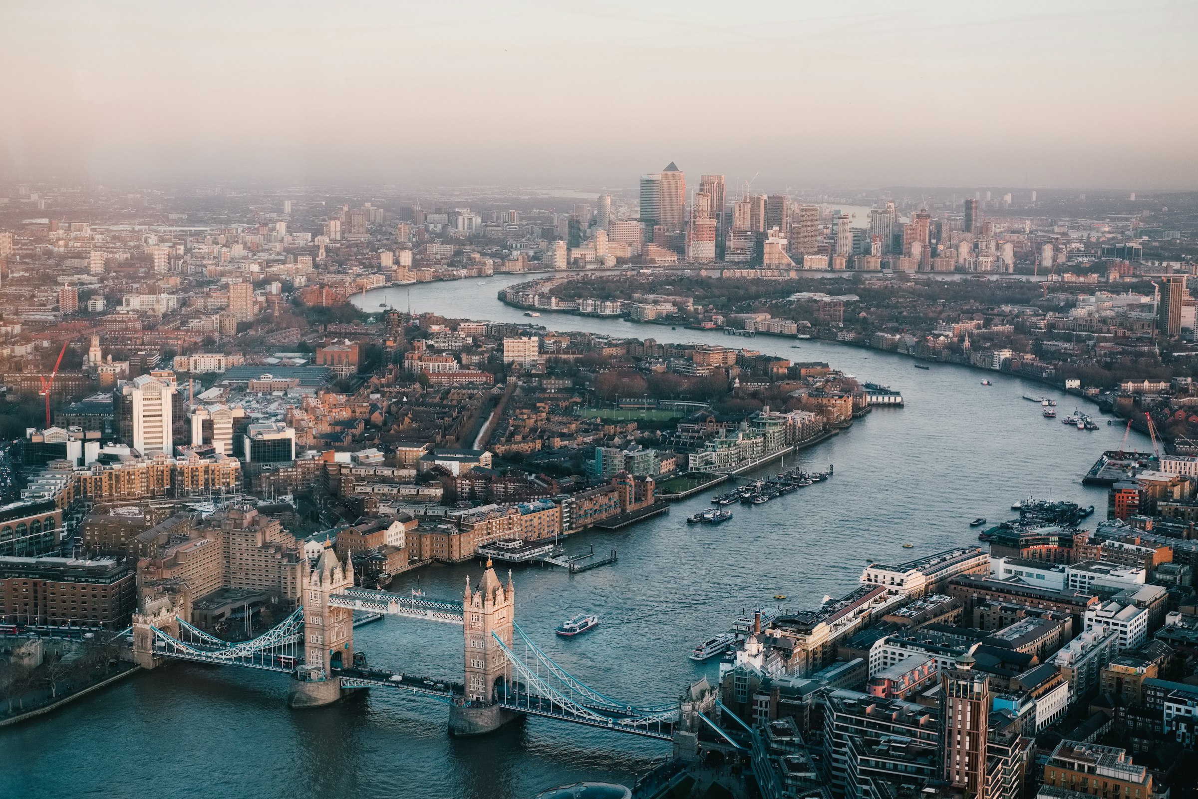 An aerial view along the River Thames through central London, with Tower Bridge in the foreground.