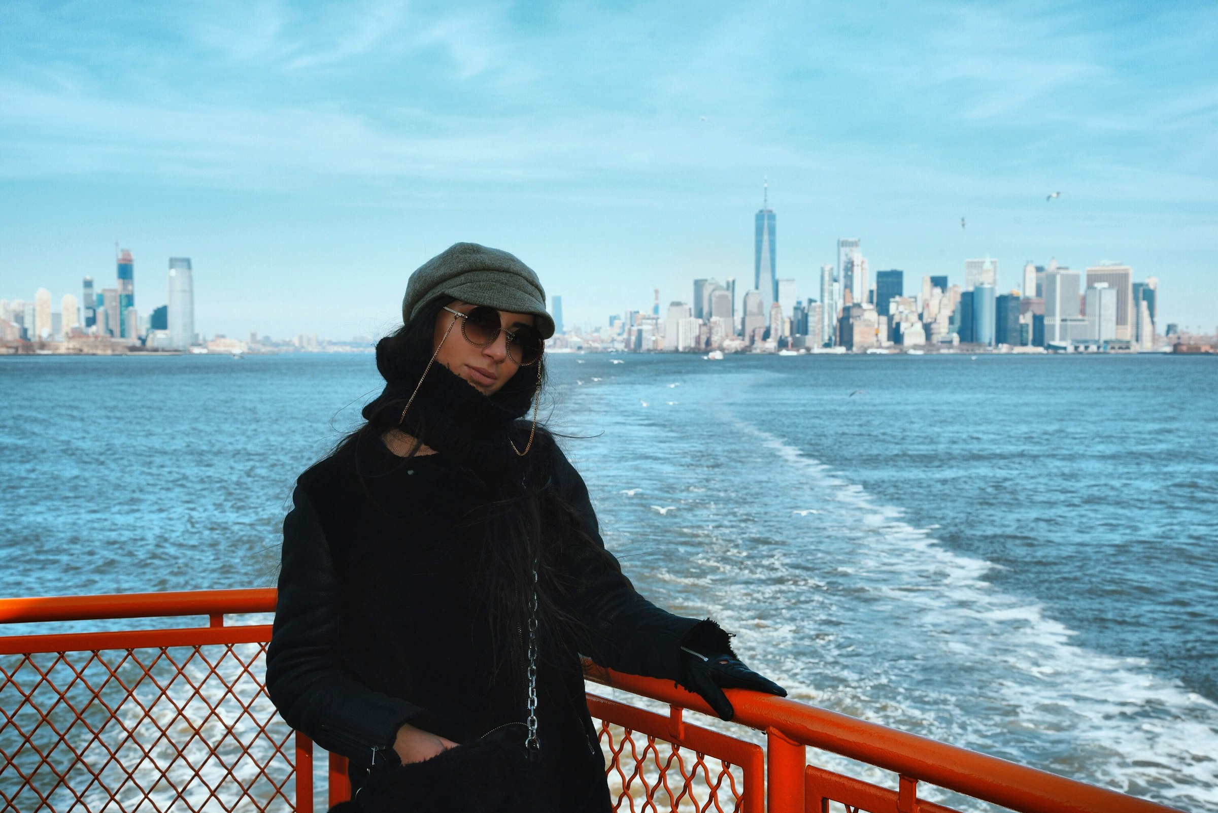 A passenger at the rail of the Staten Island Ferry with the Manhattan skyline across the water behind her.