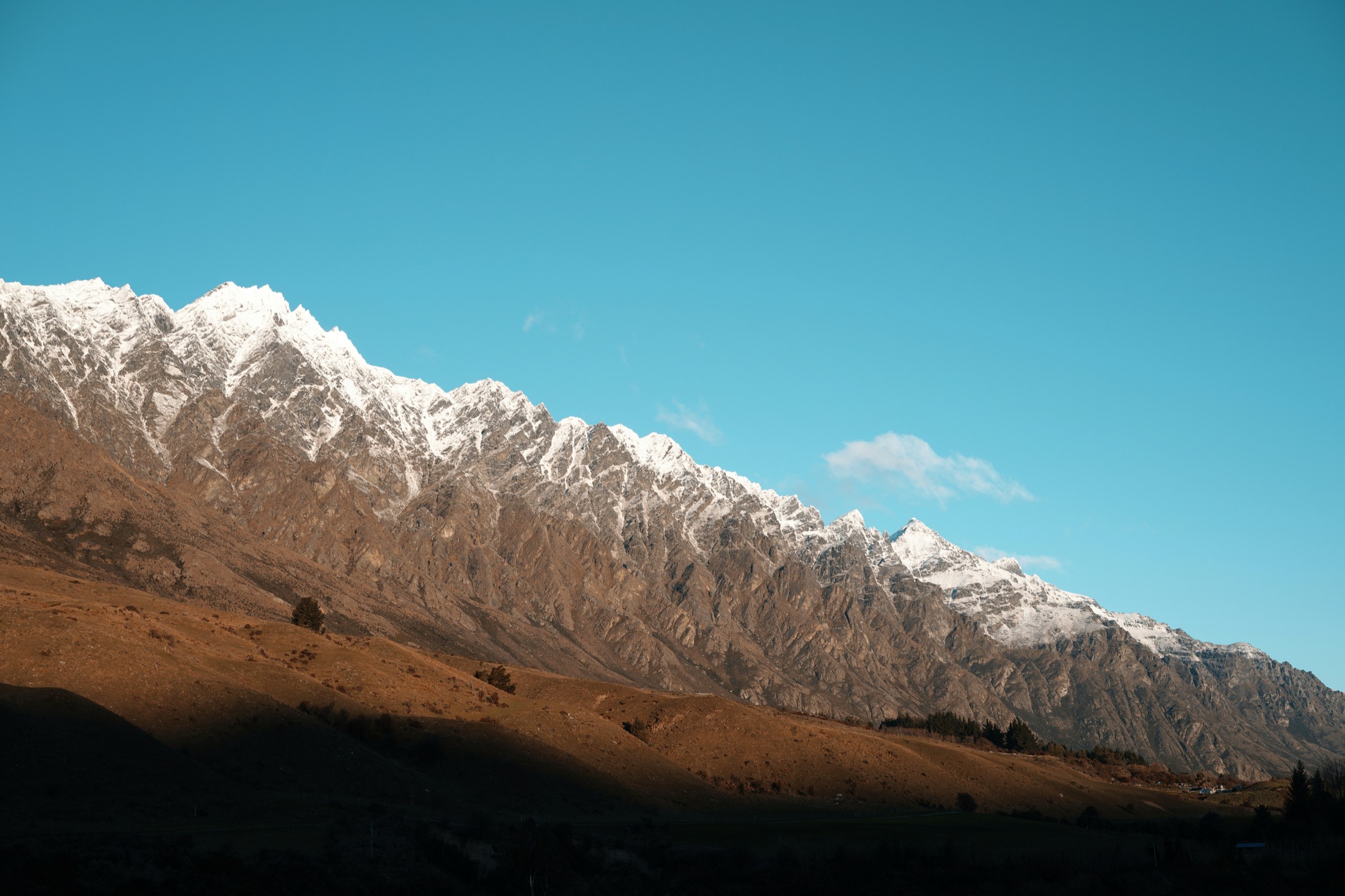The Remarkables, snow on the ridgeline, tussock slopes in shadow below.