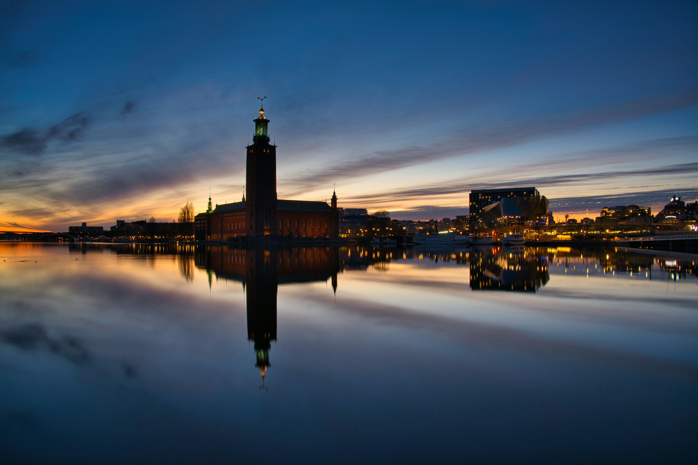 The dark tower of Stockholm City Hall silhouetted against a sunset, mirrored in still water.