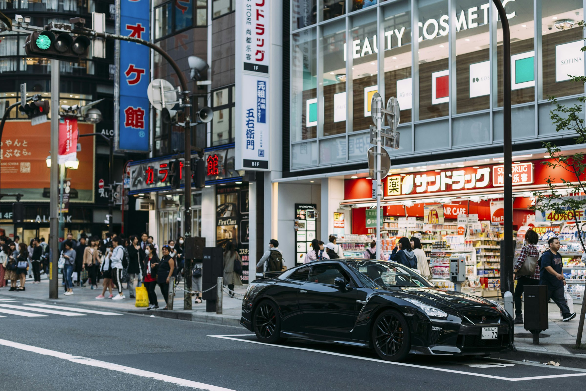 A busy Tokyo street crossing with pedestrians and shopfronts.