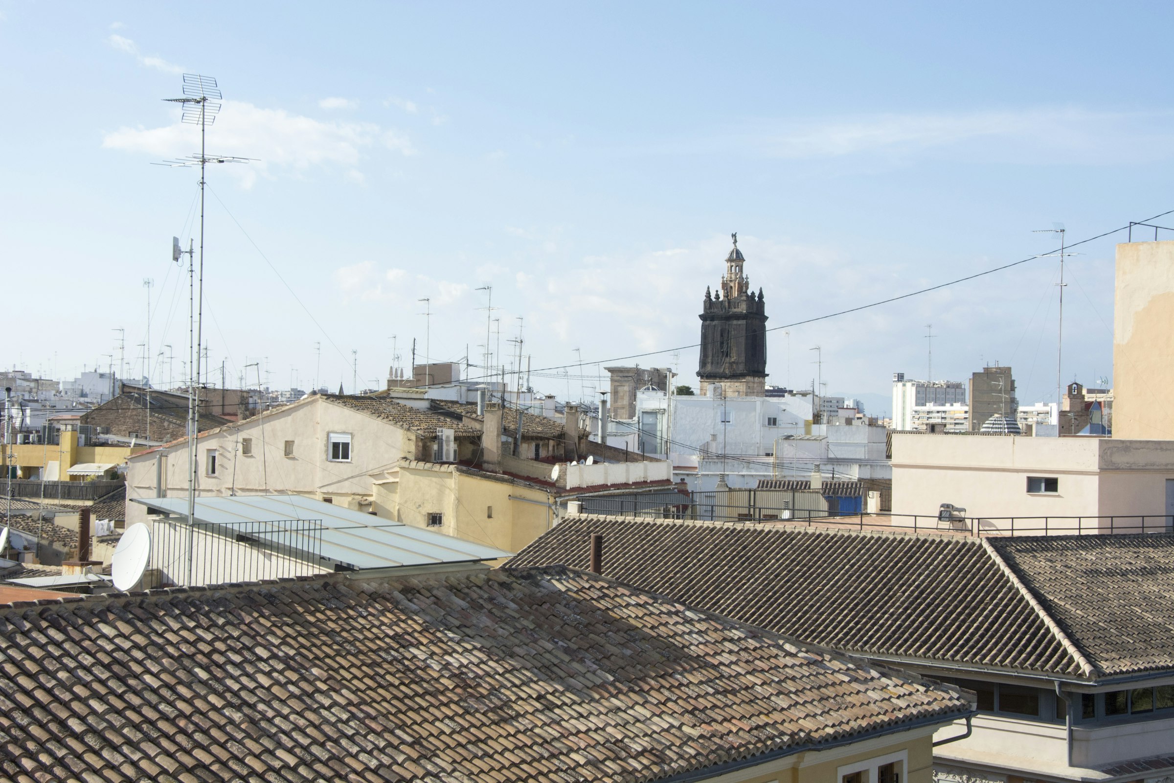 Terracotta rooftops of old Valencia with a church bell tower against a pale sky.